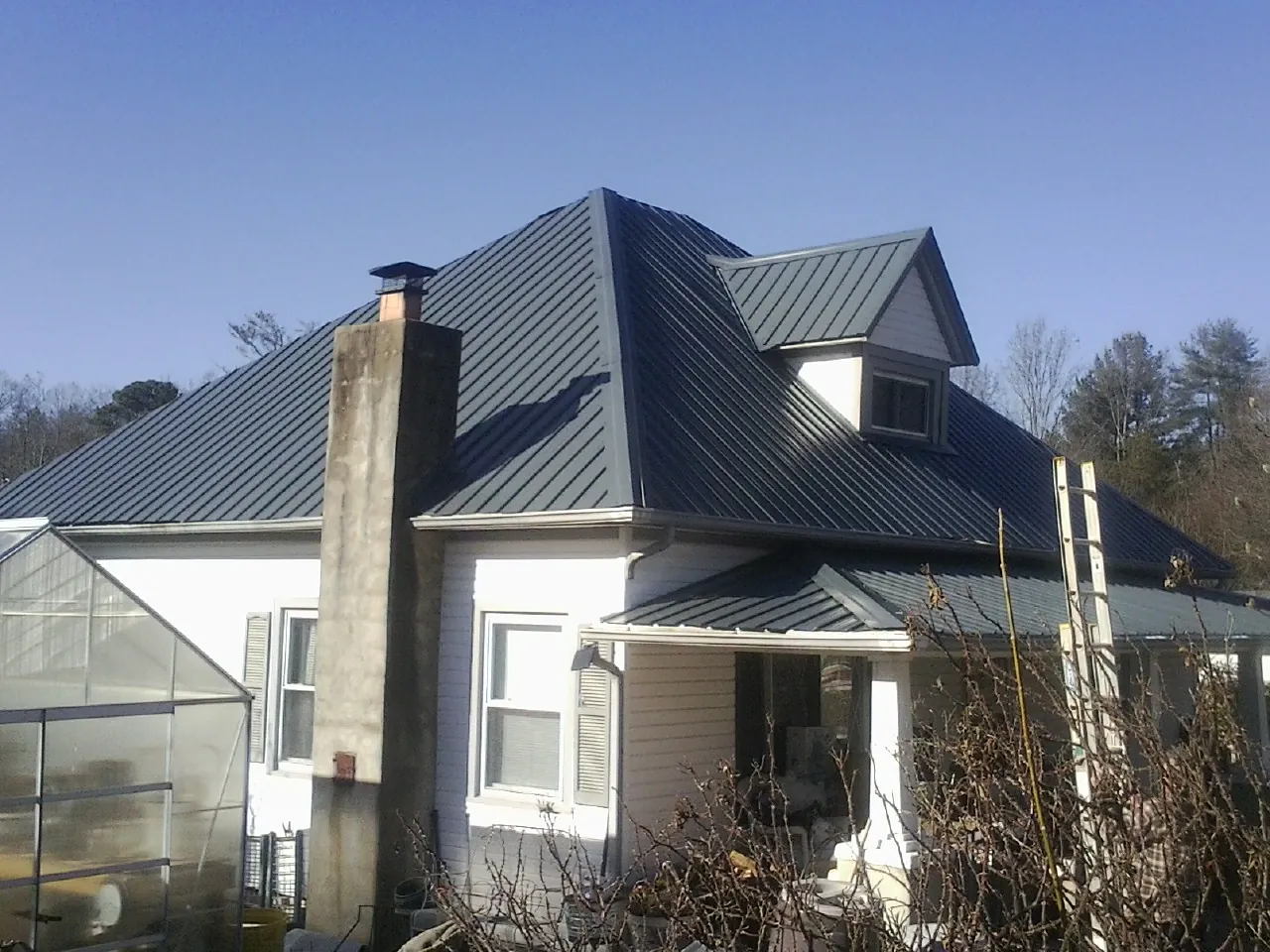 Dark blue standing seam metal roof on a white farmhouse with dormer — Slate & Tile Roof Repair by Roofing Brothers in Overbrook
