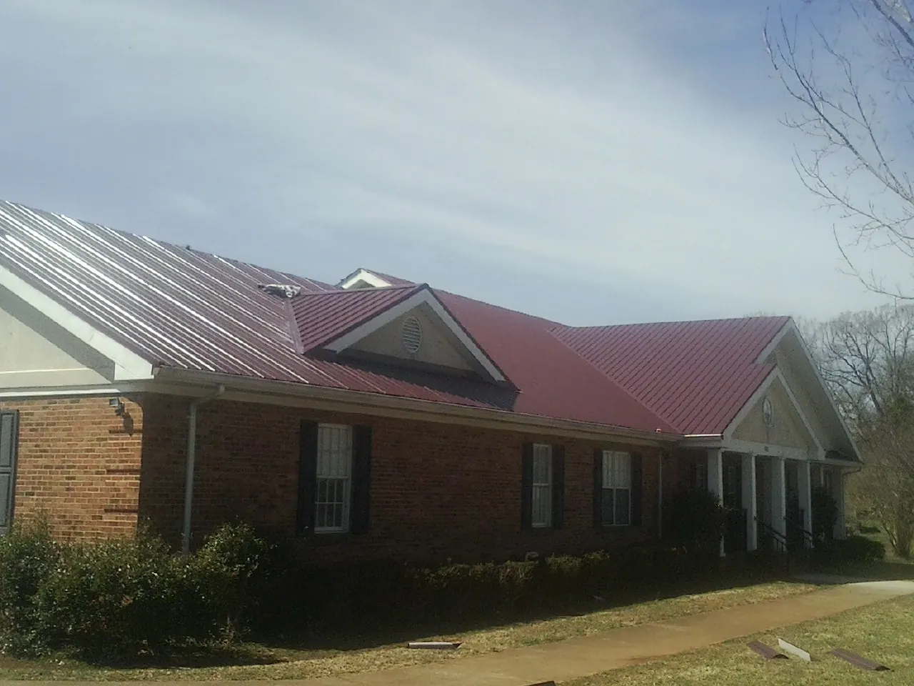Red metal roof with gabled entries on a long brick building, from a Hail Damage Roof Repair job in Overbrook