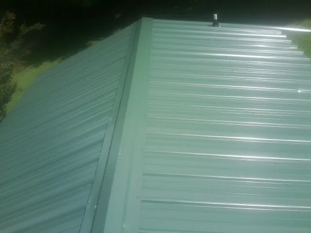 New green metal panels meeting at the ridge of a roof — Flat Roof Repair work by our crew in Overbrook
