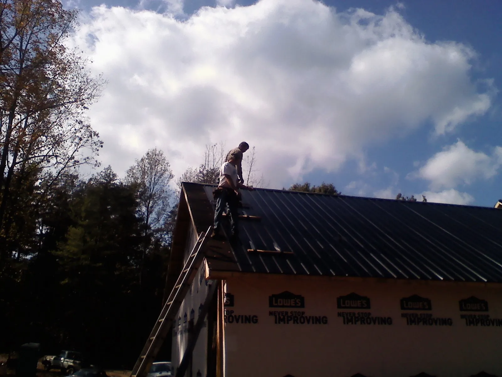 Roofer fastening dark metal panels high against a cloudy sky, from a Roof Inspection job in Overbrook