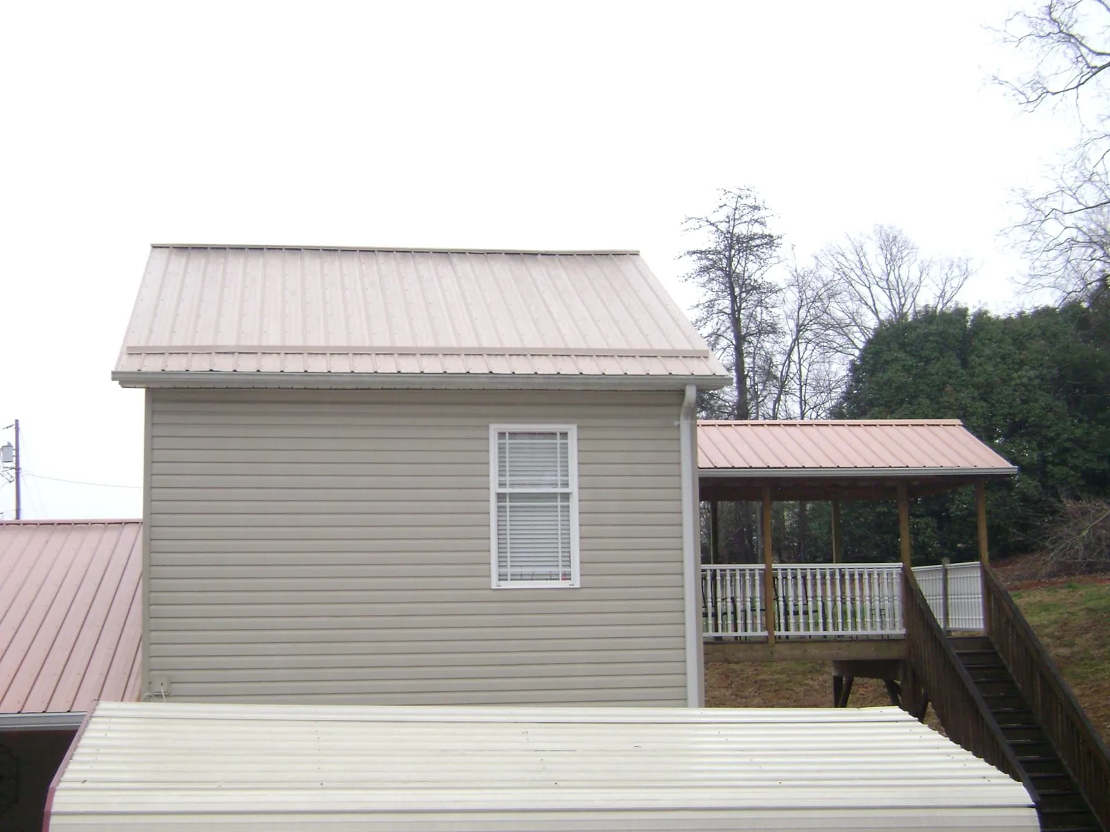 Tan metal roofs on a two story addition and attached porch, from a Roof Replacement job in Overbrook